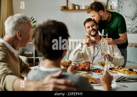 Ein schwules Paar genießt ein Abendessen mit Eltern, wobei ein Partner einen liebevollen Kuss auf den Kopf bekommt. Stockfoto