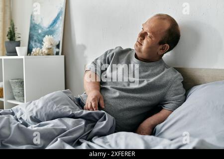 Ein Mann mit Inklusivität sitzt nachdenklich auf einem Bett, der Blick nach oben gerichtet, in der Besinnung verloren. Stockfoto