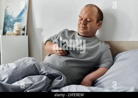 Ein Mann mit Inklusivität sitzt im Bett, benutzt sein Smartphone und beginnt seinen Tag. Stockfoto