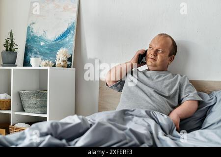 Ein Mann mit Inklusivität sitzt im Bett und spricht am Telefon. Stockfoto