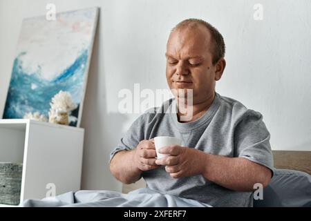 Ein Mann mit Inklusivität sitzt im Bett und hält eine Tasse Kaffee in den Händen. Stockfoto