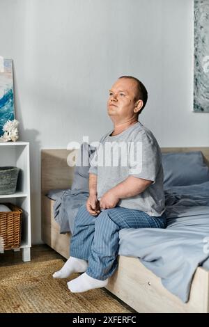 Ein Mann mit Inklusivität sitzt am Rand seines Bettes, verloren in Gedanken, während das Morgenlicht hereinströmt. Stockfoto