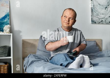 Ein Mann mit Inklusivität sitzt im Bett und genießt eine Tasse Kaffee und seine morgendliche Routine. Stockfoto