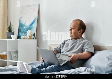 Ein Mann mit Inklusivität sitzt im Bett und benutzt seinen Laptop. Stockfoto