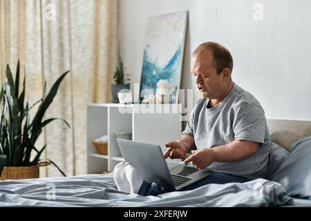 Ein Mann mit Inklusivität sitzt auf seinem Bett, vertieft in seinen Laptop. Stockfoto