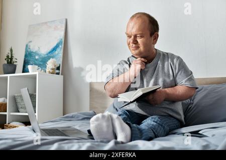 Ein Mann mit Inklusivität sitzt im Bett, hält nachdenklich ein Notizbuch und einen Stift und denkt über seinen Tag nach. Stockfoto