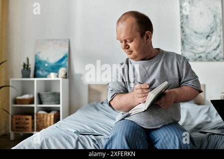 Ein Mann mit Inklusivität sitzt auf einem Bett und schreibt nachdenklich in ein Notizbuch. Stockfoto