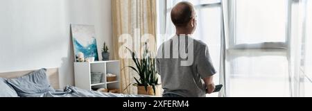 Ein Mann mit Inklusivität steht an einem Fenster in einem Schlafzimmer und blickt auf die Aussicht. Stockfoto