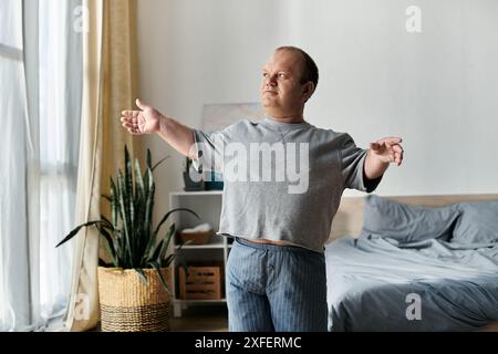 Ein Mann mit Inklusivität streckt seine Arme im Schlafanzug aus, während er am Fenster steht. Stockfoto