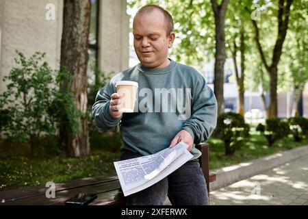 Ein Mann mit Inklusivität sitzt auf einer Parkbank, genießt seinen Kaffee und liest die Zeitung. Stockfoto