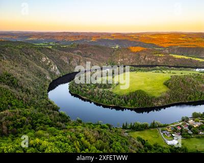 Ein malerischer Blick aus der Luft auf die Moldau-Biegung, Solenice Hufeisen, durch die tschechische Landschaft bei Sonnenuntergang. Üppige grüne Bäume und Felder rund um den Fluss, während die Sonne ein goldenes Leuchten über die Landschaft wirft. Stockfoto