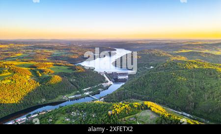 Ein Luftbild des Orlik Reservoir in Tschechien bei Sonnenuntergang zeigt einen gewundenen Fluss, Hügel und eine malerische Stadt im Tal mit leuchtendem blauem und goldenem Himmel. Stockfoto