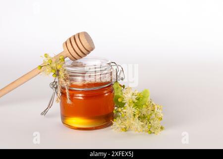 Ein Glas mit flüssigem Honig aus Lindenblüten, mit Honig und frischen Blumen auf weißem Hintergrund. Kopierbereich. Nahaufnahme Stockfoto