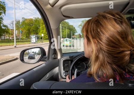 Niederlande, Frau fährt ihr Auto und schaut in den Seitenspiegel, der vor bevorstehenden anderen Fahrzeugen oder Motorrädern warnt. Stockfoto