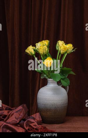 Ein schöner Blumenstrauß aus gelben Rosen in einer grauen Vase auf einem Hintergrund aus dunkelbraunem Stoff. Platz für Text, Kopierraum Stockfoto