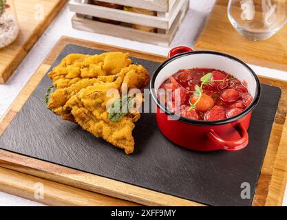 Paniertes Fleisch mit Tomatensalat auf schwarzem Schiefertablett am Restauranttisch Stockfoto