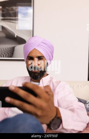 Mit dem Smartphone, Mann im Turban, der sich zu Hause auf der Couch entspannt Stockfoto