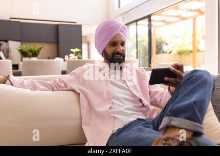 Entspannen auf der Couch, Mann im Turban mit Smartphone zu Hause Stockfoto