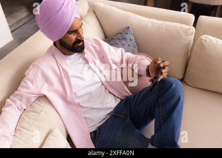 Entspannen auf dem Sofa, Mann in rosa Turban mit Smartphone zu Hause Stockfoto