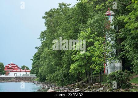 Alter Leuchtturm am Meer zwischen Bäumen vor dem Hintergrund von alten Gebäuden und Böschungen Stockfoto