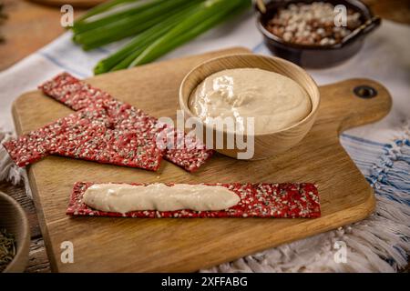 Eine Schüssel Hummus mit roten Rote-Bete-Crackern, die auf einem rustikalen Holzschneidebrett sitzen Stockfoto
