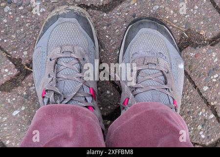 Alte abgenutzte Schuhe, Wanderschuhe auf weiblichem Fuß auf dem Boden, Anzeichen von Abnutzung, die zu Charakter beitrugen, Armut und Obdachlosigkeit, viele Kilometer gingen weiter Stockfoto