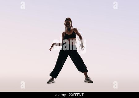 Frau tanzt in einem Studio, zeigt Fitness und Flexibilität. Energiegeladen und dynamisch strahlt sie Selbstvertrauen aus, während sie einen Sport-BH und eine Hose trägt. Stockfoto