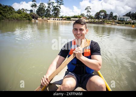 Junger Mann in Schwimmweste rudert ein kleines Boot auf einem See Stockfoto