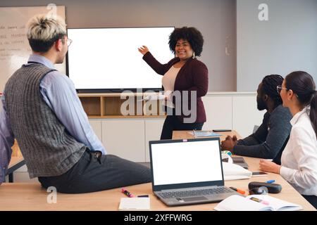 Afro Latina-Frau, die vor dem Bildschirm im Büro steht und ihren Kollegen und Partnern, ihren Kollegen, verschiedene Themen in Geschäftstreffen vorstellt Stockfoto