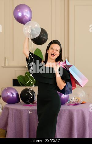 Frau posiert mit Ballons und Geschenktüten. Porträt eines schönen Geburtstagskindes Stockfoto