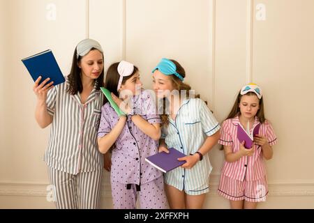 Eine Frau und drei Mädchen im gestreiften Pyjama halten Bücher, interagieren und lächeln an einer einfachen Wand. Stockfoto