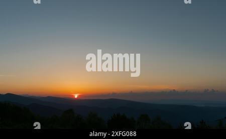 Sonnenuntergang über einer bergigen Landschaft mit klarem Himmel. Stockfoto