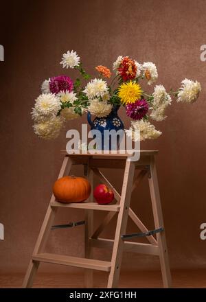 Bouquet aus weißen, orangen, roten Chrysinthen in einer Vase. Blaue Kanne aus Steingut mit weißen Gänseblümchen und einem Griff. Buntes Herbststrauß auf einem hölzernen s Stockfoto