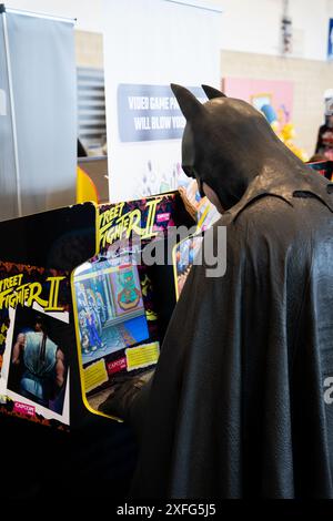 HARROGATE, GROSSBRITANNIEN - 22. JUNI 2024. Ein männlicher Cosplayer verkleidet als Batman und spielt eine Retro-Spielekonsole von Street Fighter in einem lustigen Comic-Betrügerbild Stockfoto