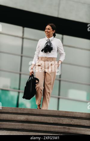 Die lächelnde Latina-Geschäftsfrau schreitet selbstbewusst durch die Straßen der Stadt. Stockfoto