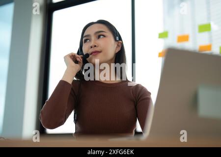 Junge Frau, die in einem modernen Büro mit Headset und Laptop arbeitet und Kundensupport bietet Stockfoto