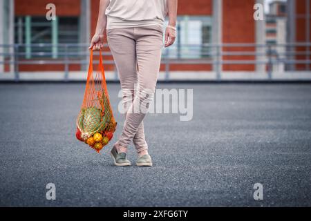 Frau mit wiederverwendbarer Netztasche nach dem Einkaufen in der Stadt. Kein Abfall und kein Kunststoff, nachhaltiger Lebensstil Stockfoto