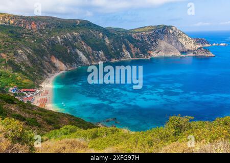 Petani Beach, Lixouri im Sommer, auf der Ionischen Insel Kefalonia, Griechenland, mit orangefarbenen Sonnenschirmen, Sonnenliegen, blauem Himmel und hohen Bergen. Platz für Co Stockfoto
