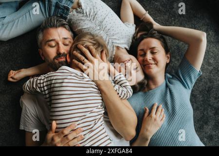 Direkt über der Aufnahme von Eltern, die Sohn und Tochter umarmen, während sie zu Hause auf dem Boden liegen Stockfoto