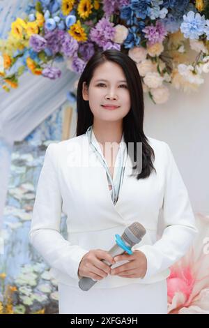 Elegante asiatische Frau in weißem Anzug, die das Publikum mit farbenfrohem floralem Hintergrund anspricht Stockfoto