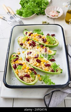 Zucchini gefüllt mit Petitim, roten Bohnen, Mais mit Basilikum und Soße, gebacken auf einem alten, zerrissenen Fliesenhintergrund. Draufsicht. Stockfoto