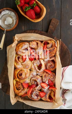 Erdbeerrollies Blätterteig mit Pudding innen und mit Puderzucker auf rustikalem Holztisch bestreut. Rezeptidee für das Sommerfrühstück. Abdeckung oder AR Stockfoto