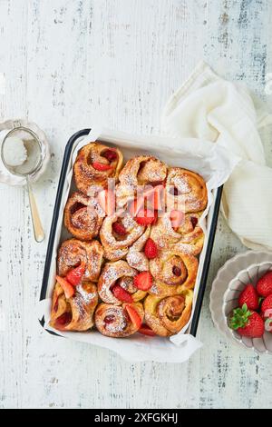 Erdbeerrollies Blätterteig mit Pudding innen und mit Puderzucker bestreut auf weißen rustikalen Holztisch. Rezeptidee für das Sommerfrühstück. Abdeckung Stockfoto