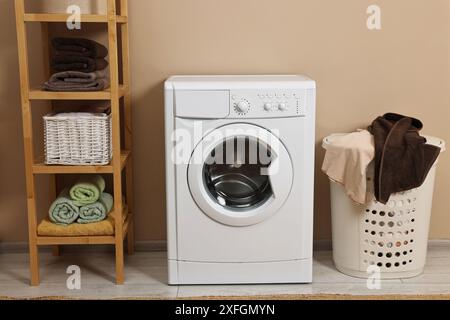 Waschmaschine, Korb und Regal in der Nähe beigefarbener Wände im Innenbereich Stockfoto