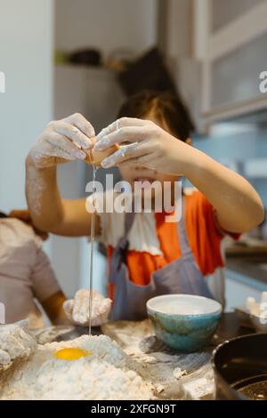 Ein Mädchen, das Ei in Mehl bricht, während er zu Hause backen will Stockfoto