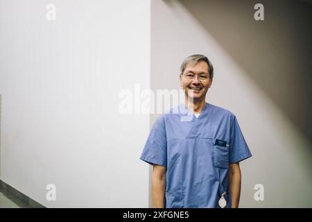 Porträt eines lächelnden männlichen Seniorarztes, der im Krankenhaus in der Nähe der Wand steht Stockfoto