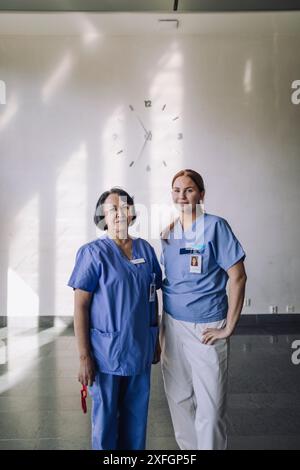Porträt einer leitenden Ärztin, die mit einer jungen Praktikantin vor der Wand im Krankenhaus steht Stockfoto
