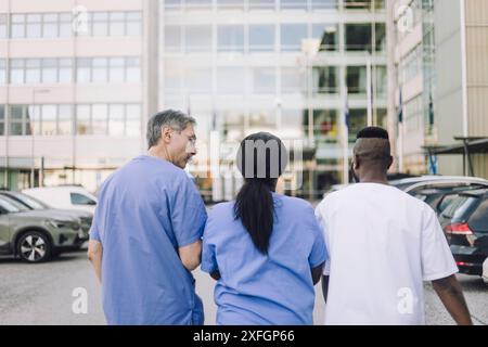 Rückansicht männlicher und weiblicher medizinischer Fachkräfte, die während des Spaziergangs zum Krankenhausgebäude diskutieren Stockfoto