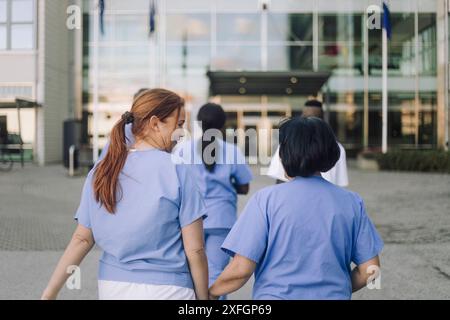 Weibliche Auszubildende spricht mit einem leitenden Arzt, während sie in Richtung Krankenhausgebäude geht Stockfoto