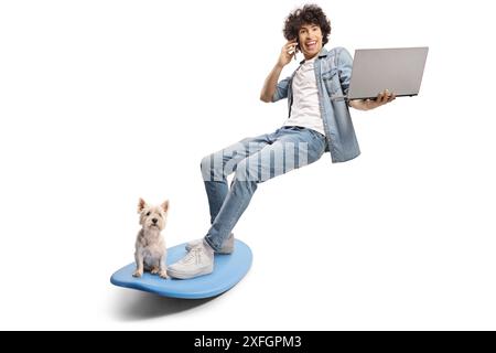 Junger Mann und Hund auf einem Surfbrett und mit einem Smartphone und Laptop isoliert auf weißem Hintergrund Stockfoto